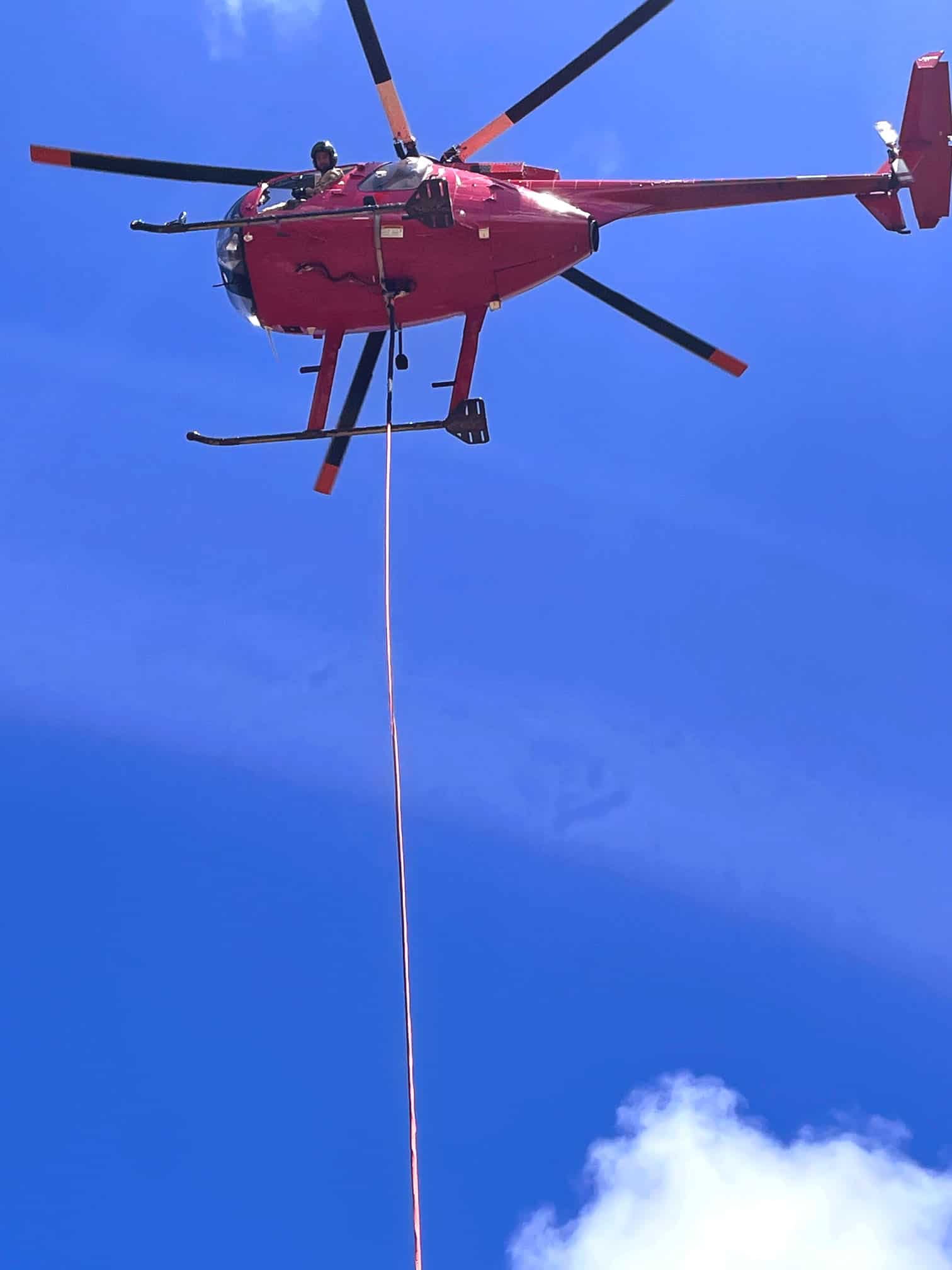 A man looks out of a utility helicopter with a long line attached to it