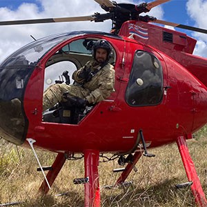 A man sits in a utility helicopter that is sitting on the ground