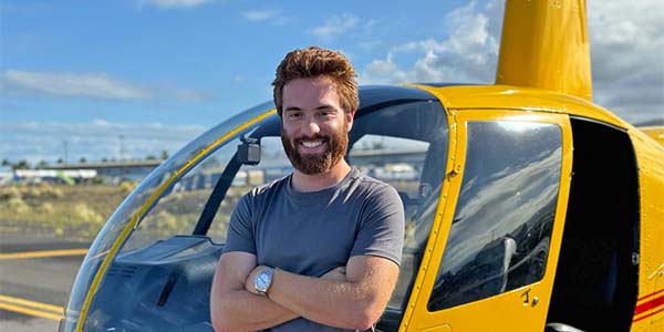 A smiling man with his arms crossed stands in front of a helicopter