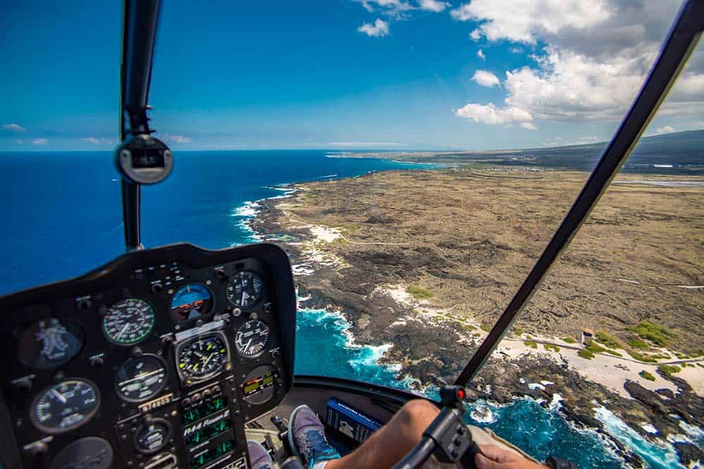 A view from inside a helicopter's cockpit while flying over a coastline on a clear day