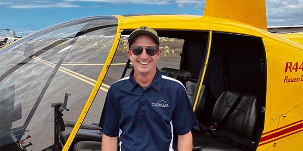 A smiling man leans against a yellow helicopter.