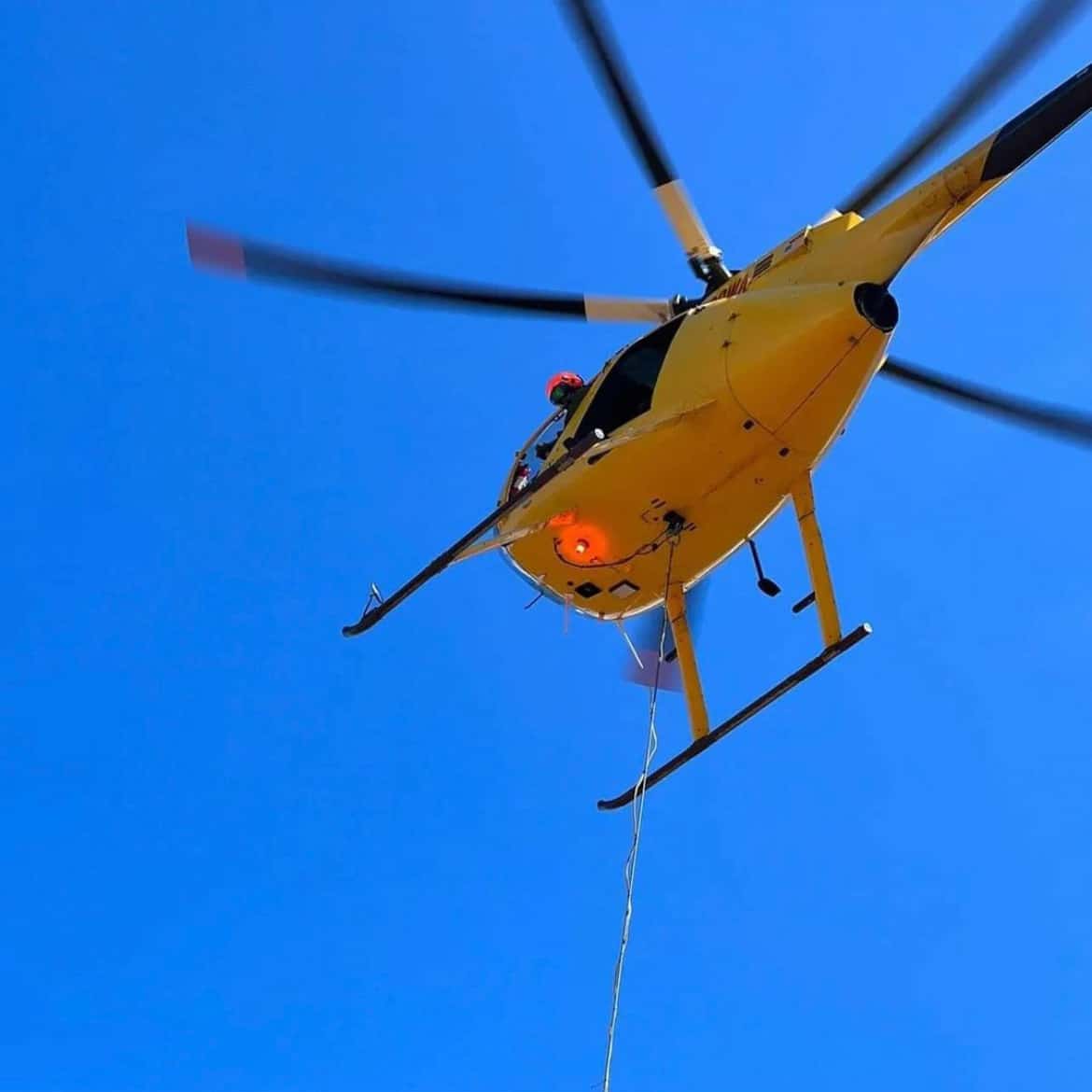 A helicopter with a long line hanging from it flies overhead