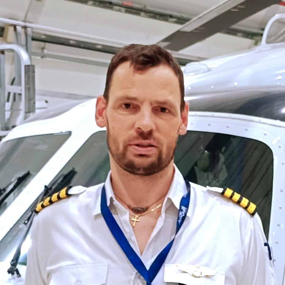 A man in a captain's uniform stands in a hangar in front of a helicopter