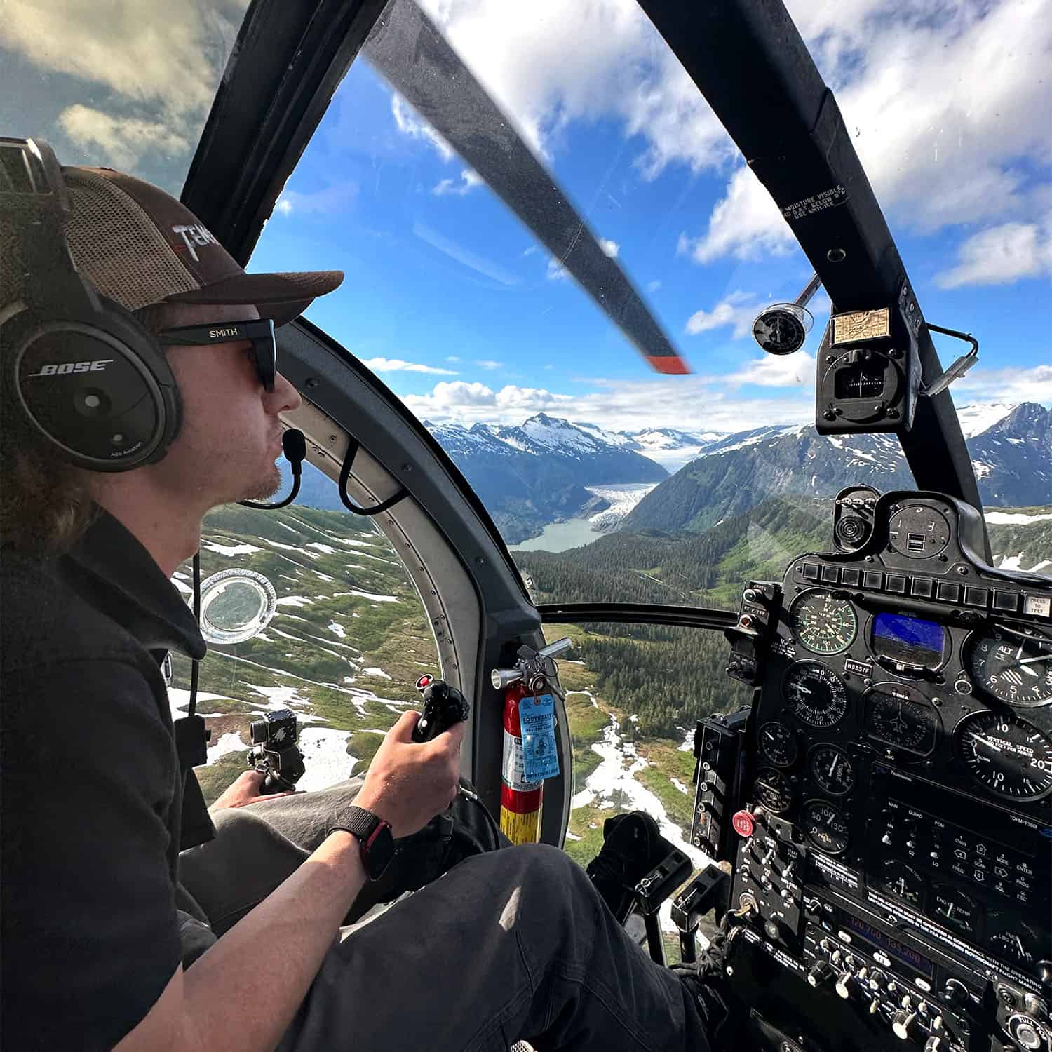 A man flies in a helicopter over snow-capped mountains and a glacier