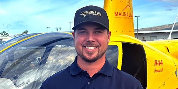 A smiling man in a Robinson Helicopters hat stands in front of a helicopter