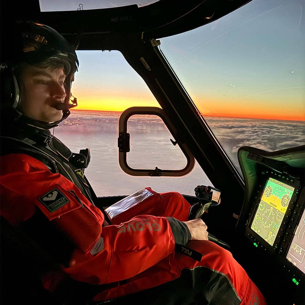 A person in a flight suit flies above some clouds at sunset.