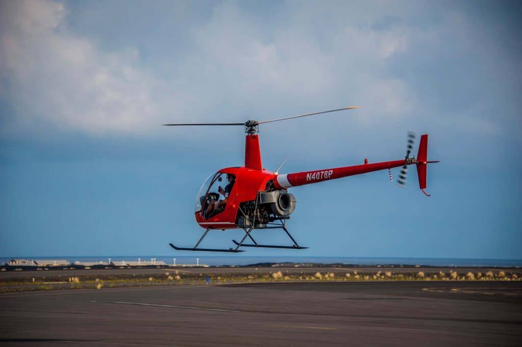 A red helicopter hovers above the runway