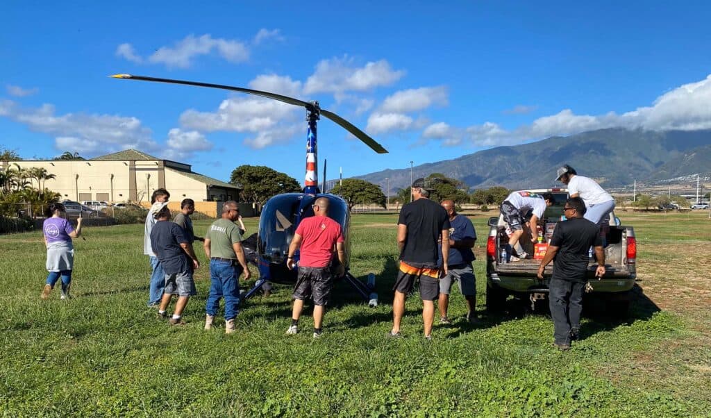 A line of people move supplies from a parked helicopter to a waiting pickup truck