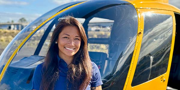 A smiling person stands in front of a helicopter