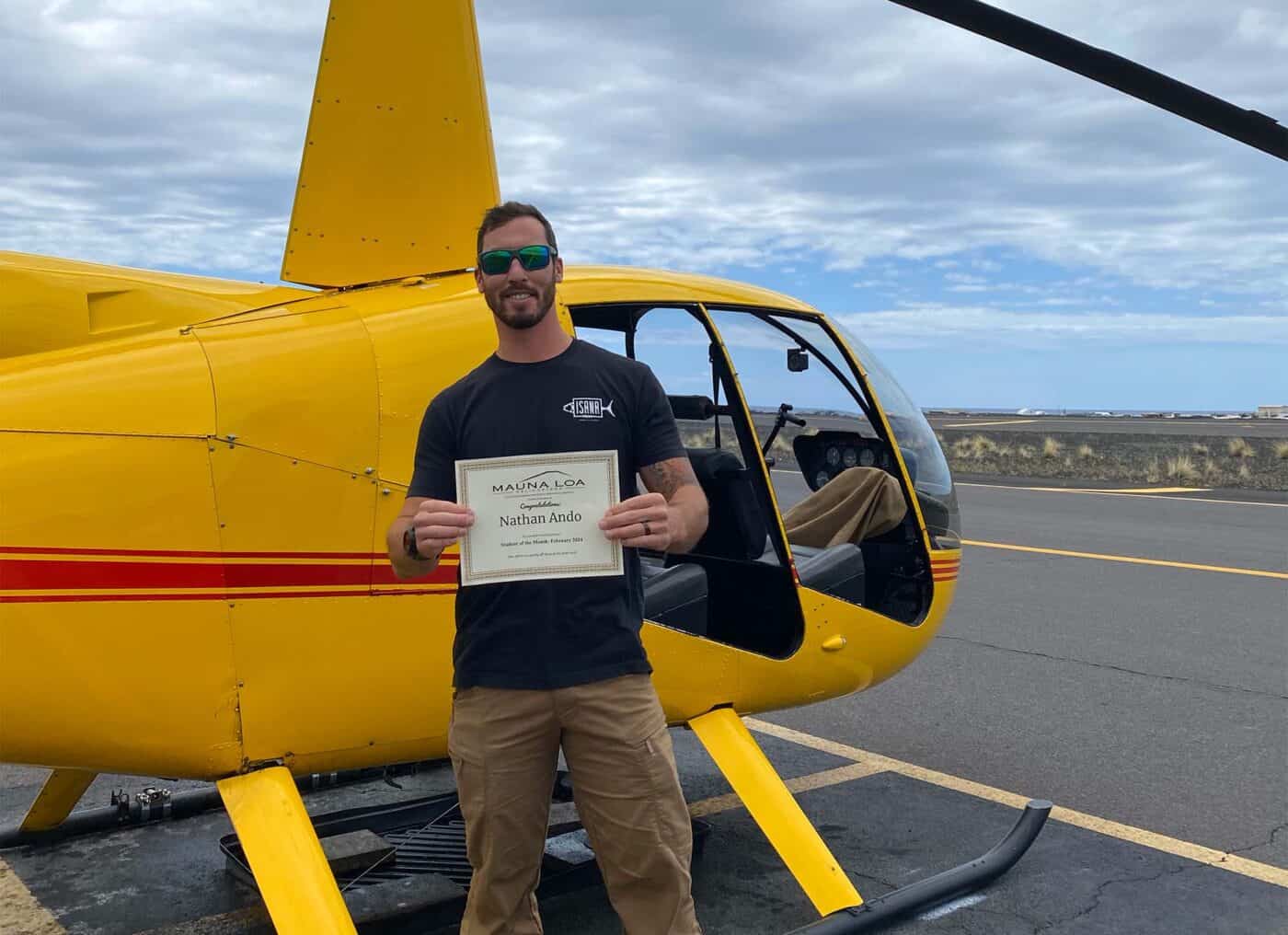 A smiling man holds a certificate while standing in front of a helicopter