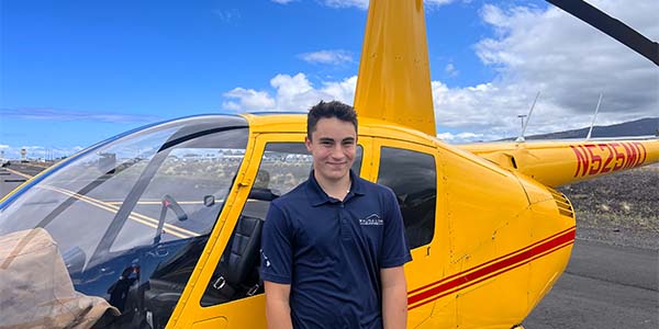 A smiling person stands in front of a parked helicopter