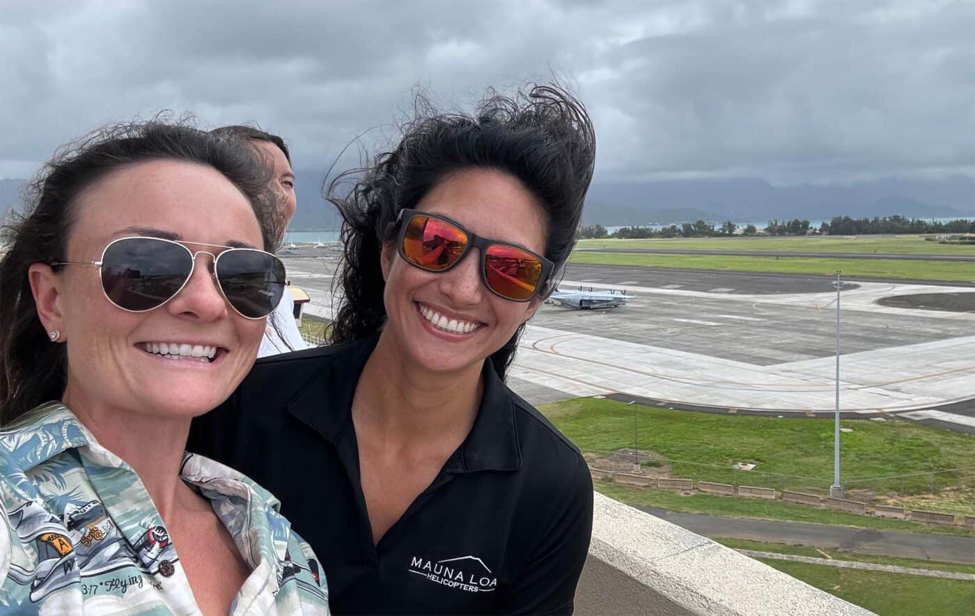 Two smiling people pose for a selfie while looking over an airport.