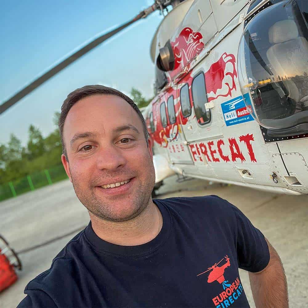 A man stands in front of a helicopter and takes a selfie