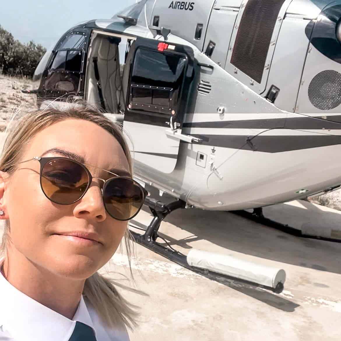 A woman stands in front of a helicopter and takes a selfie