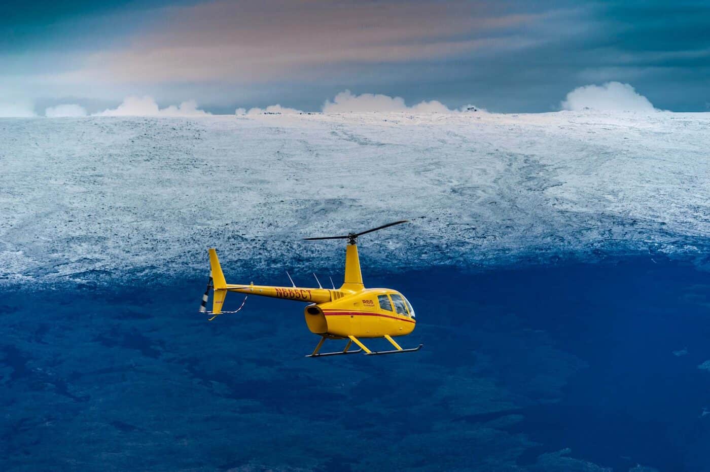 A helicopter flies over some snow-capped mountains