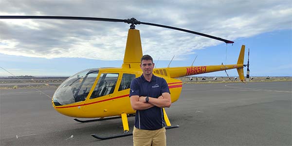 A man stands in front of a parked helicopter with his arms crossed.