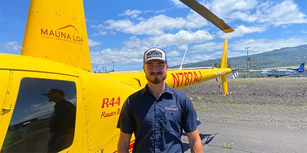 A smiling man stands in front of a parked helicopter