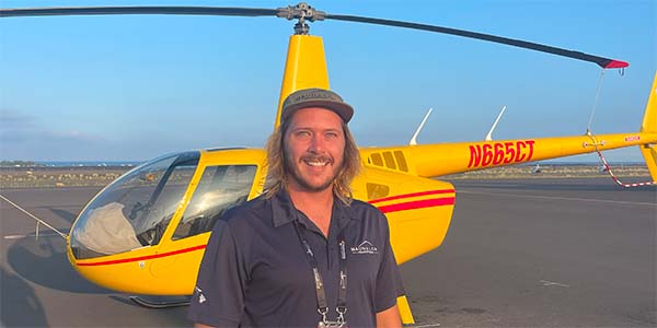 A smiling man stands in front of a parked helicopter