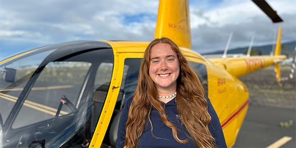 A smiling woman stands in front of a parked helicopter