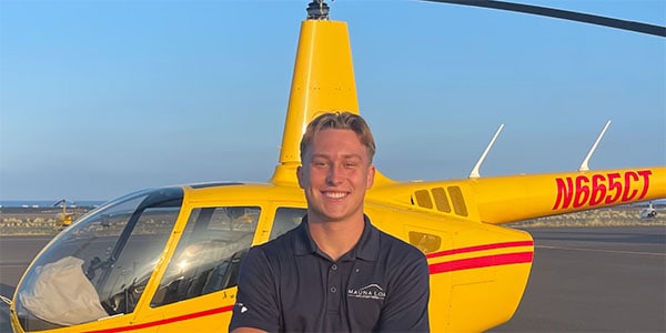 A smiling person stands in front of a parked helicopter