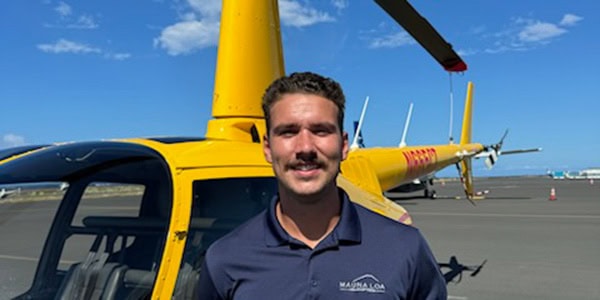 A smiling person stands in front of a parked helicopter