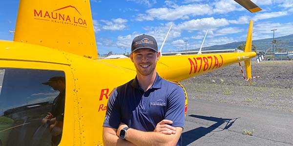 A smiling person stands in front of a parked helicopter