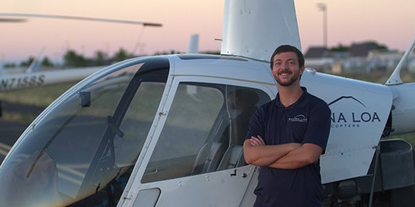 A smiling person stands in front of a parked helicopter