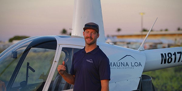 A smiling person stands in front of a parked helicopter