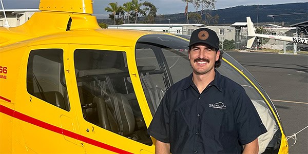 A smiling person stands in front of a helicopter